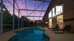 En indendørs swimmingpool med glasloft, omgivet af liggestole og udsigt til himlen.