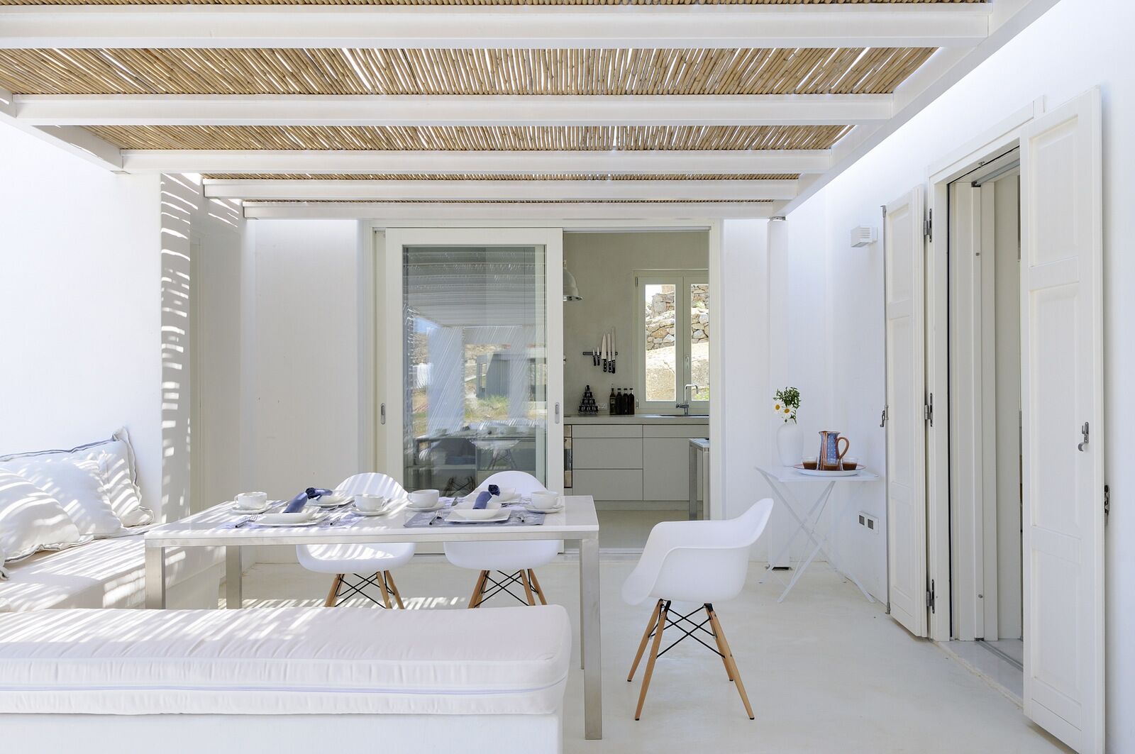 A modern, minimalist bedroom with a glass dining table, a white sofa, and a small white chair.