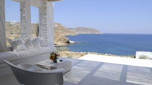 Un espace extérieur moderne, aménagé avec un mobilier blanc, offrant une vue sur la mer et un paysage rocheux.