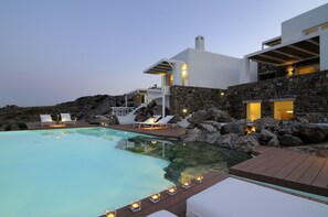 A modern villa with a swimming pool, stone walls, and outdoor seating. - Inviting 7-bed Villa in Mikonos - Villa Jackie (Mykonos)