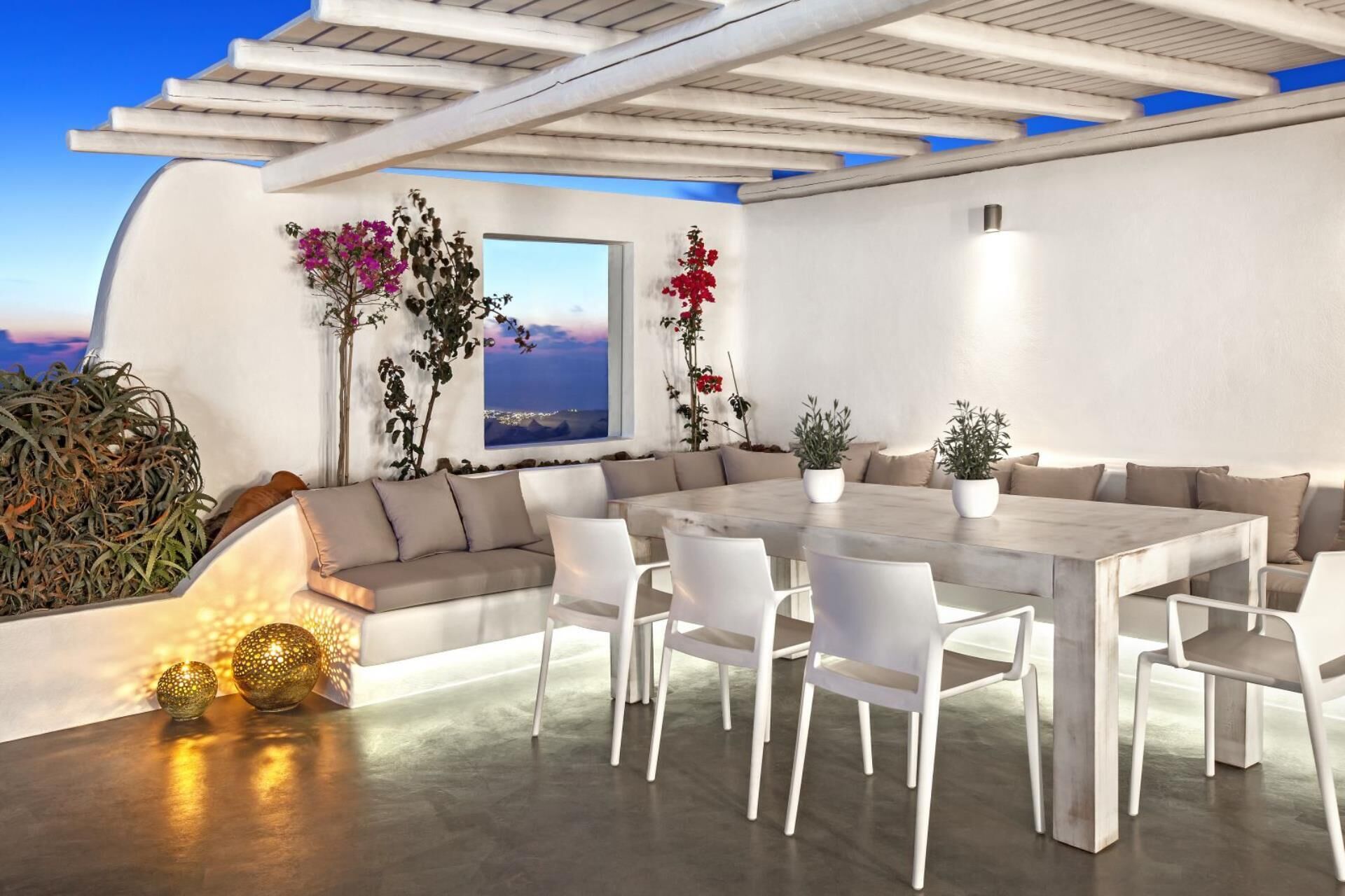 A modern outdoor dining area with a white table and chairs, surrounded by a white wall and a pergola.