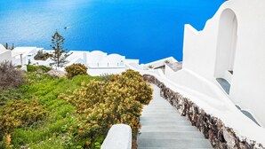 Un bâtiment blanc avec un escalier menant à un balcon d’où l’on peut admirer une mer bleue et des îles lointaines.