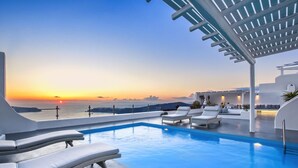 Une piscine sur le toit, dotée de chaises longues et offrant une vue sur le coucher de soleil sur la mer.