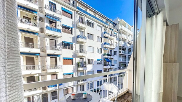 A balcony with a table and chairs, overlooking a multi-story residential building with balconies.
