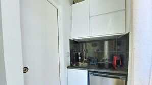 A compact kitchen with white cabinets, a stainless steel refrigerator, and a black countertop.