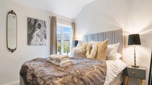 Una camera d'albergo con un letto grande, un comodino con una lampada, una finestra con tende e un quadro appeso al muro.