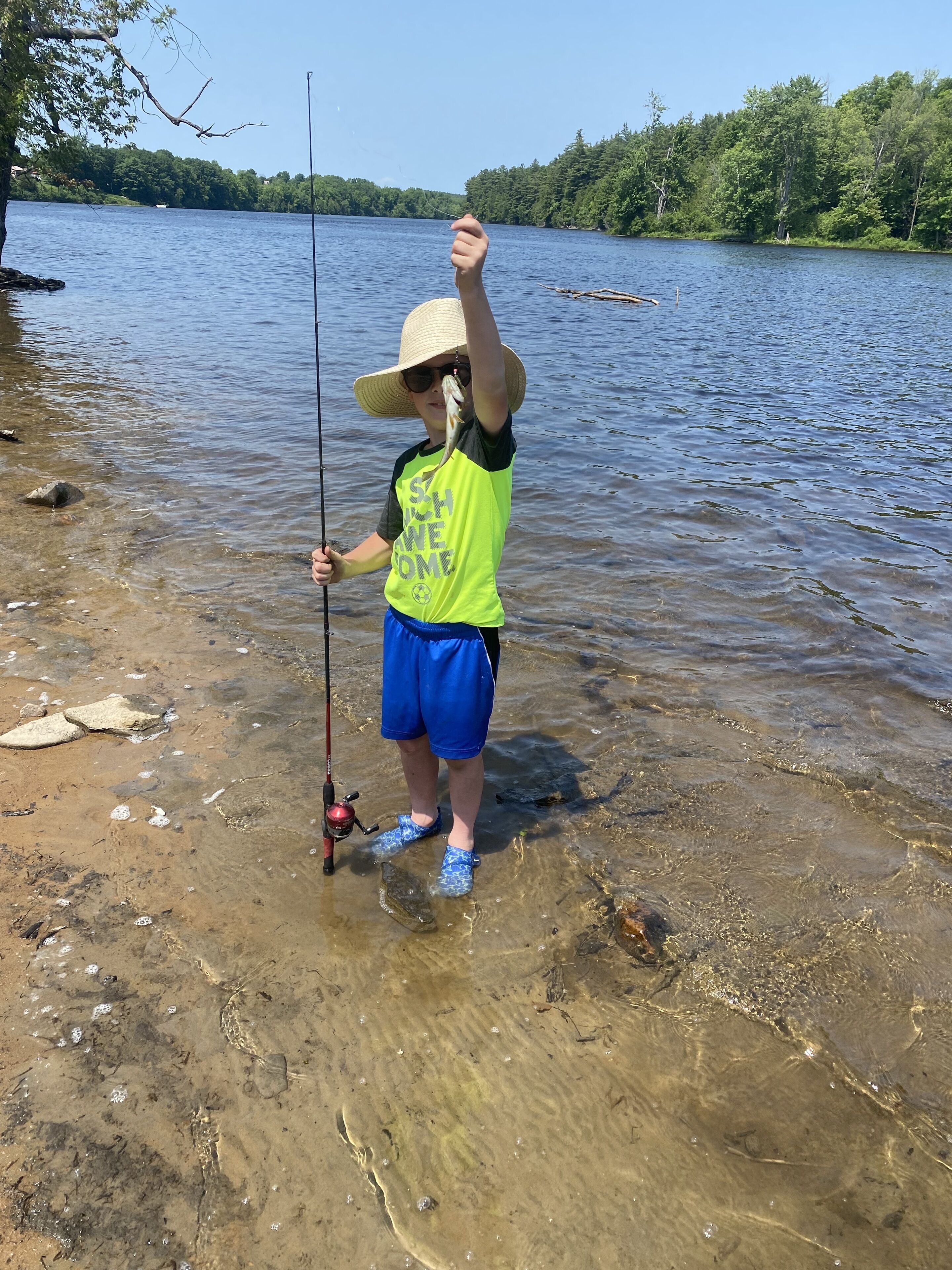 Une personne se tient au bord d’un lac, tenant une canne à pêche.