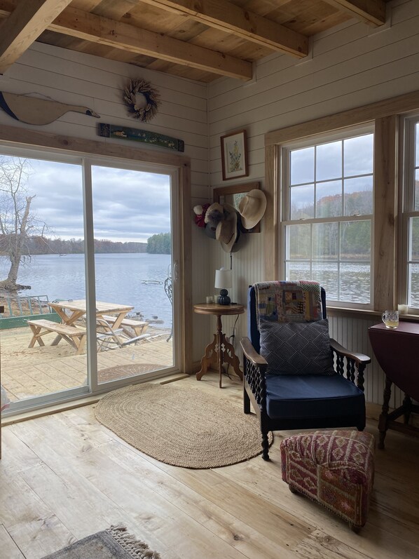 A cozy cabin with a large window overlooking a lake, wooden furniture, and a rustic interior.