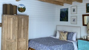 Una camera da letto con soffitto in legno, un letto con copriletto decorato, un armadio in legno e un piccolo tavolo con lampada.