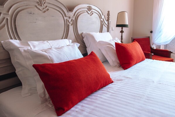 A neatly made bed with white and red pillows, a wooden headboard, and a bedside lamp.