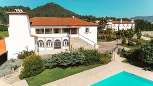 A white building with a red-tiled roof, a swimming pool, and a hillside in the background. - Quinta do Convento Val Pereiras (Ponte de Lima)