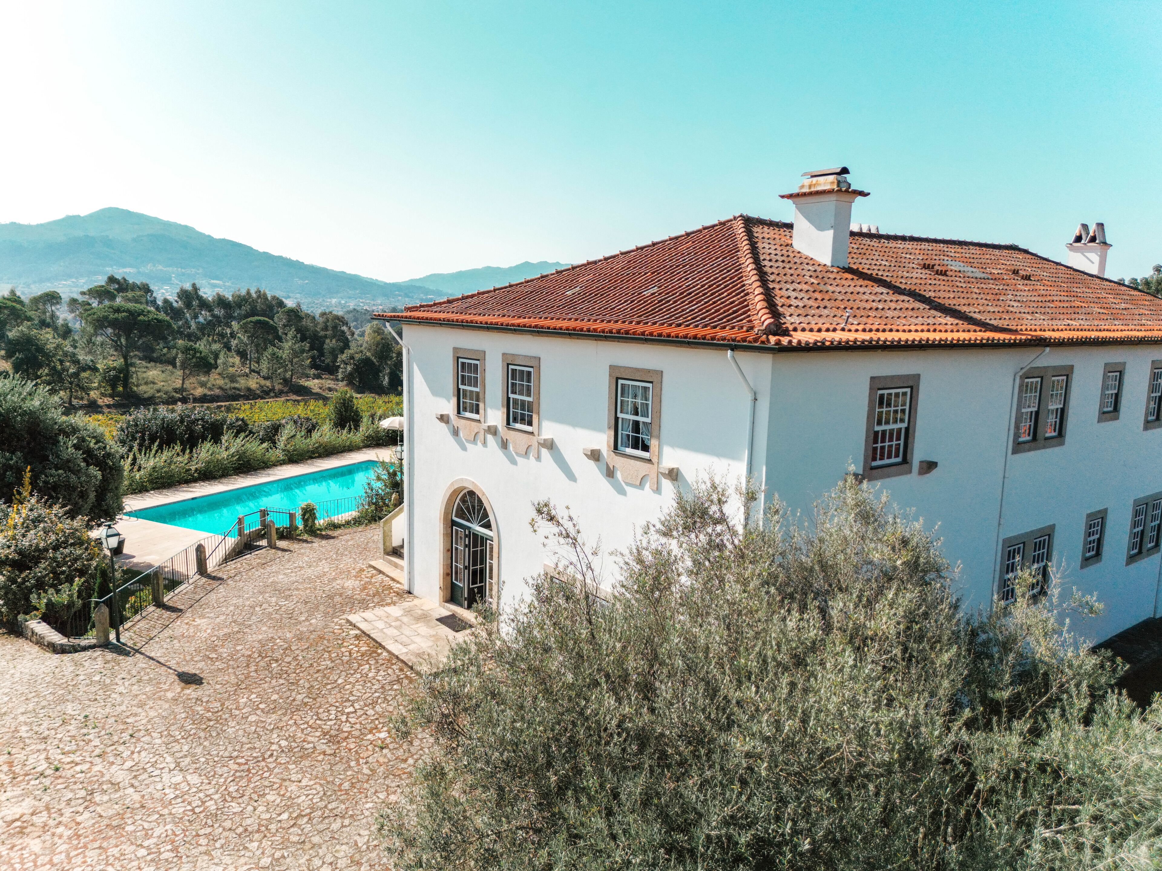 A white villa with a tiled roof, a swimming pool, and a stone pathway leading to the entrance.