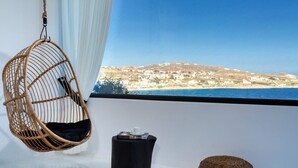 A wicker hanging chair by a window with a view of a coastal landscape. - Captivating 5-bed Villa in Mikonos Giullietta (Mykonos)
