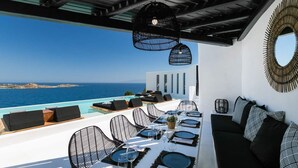 A dining area with a view of the sea, outdoor seating, and hanging lights. - Captivating 5-bed Villa in Mikonos Giullietta (Mykonos)