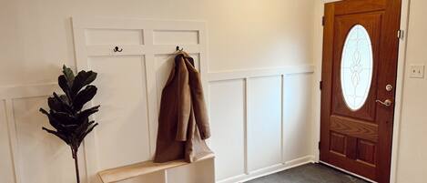 A hallway with a wooden bench, a potted plant, and a door with a stained glass window.