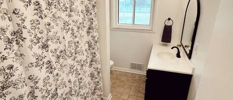 A bathroom with a shower curtain, a window, a sink, and a mirror.