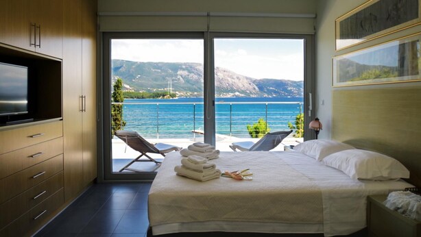 A bedroom with a bed, a TV, and a balcony with a view of the sea and mountains.