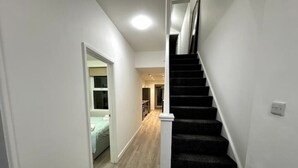 Eine Treppe mit Teppichhandlauf führt zu einem Schlafzimmer mit Bett und Fenster.
