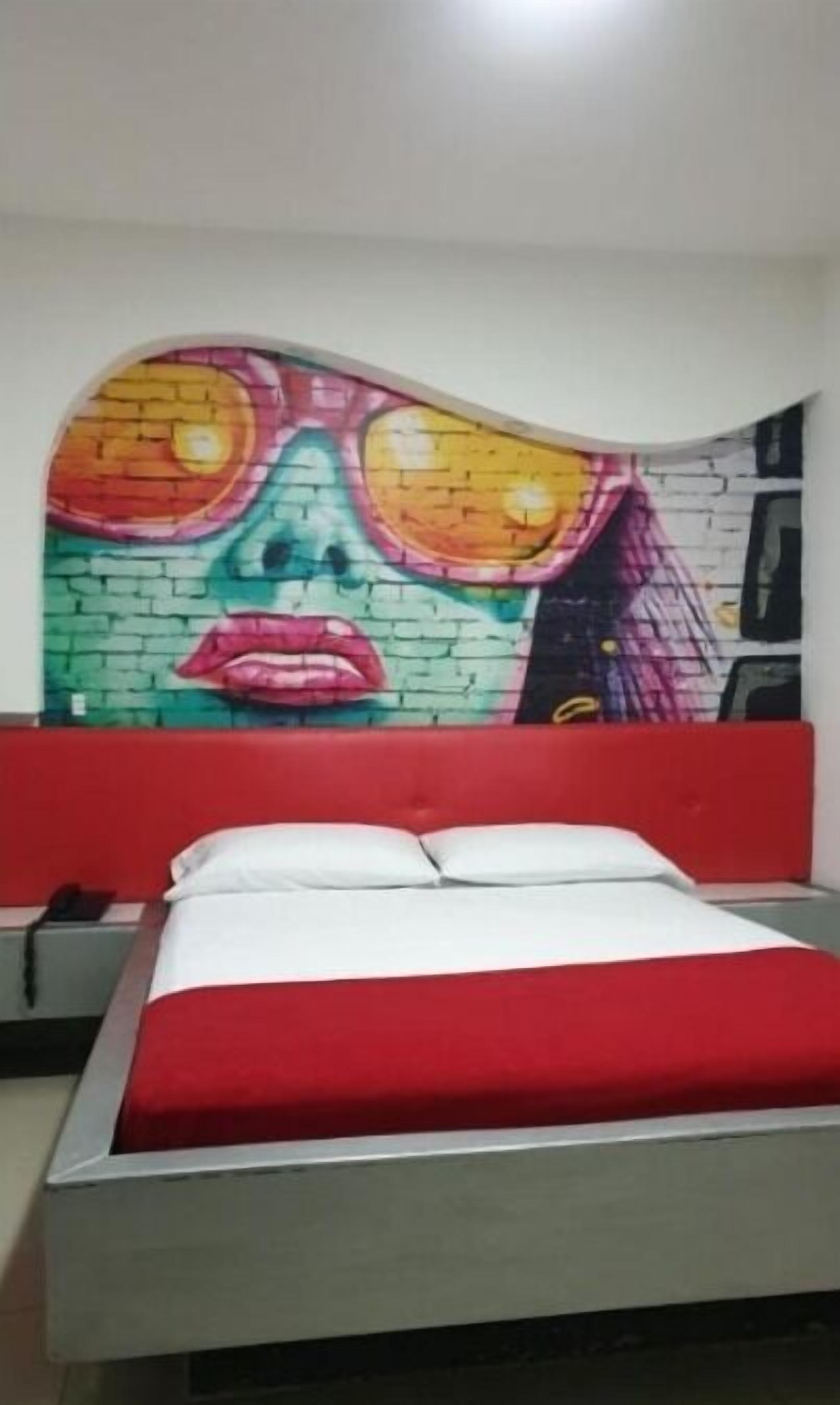 A room with a bed, a red headboard, and a colorful mural on the wall.