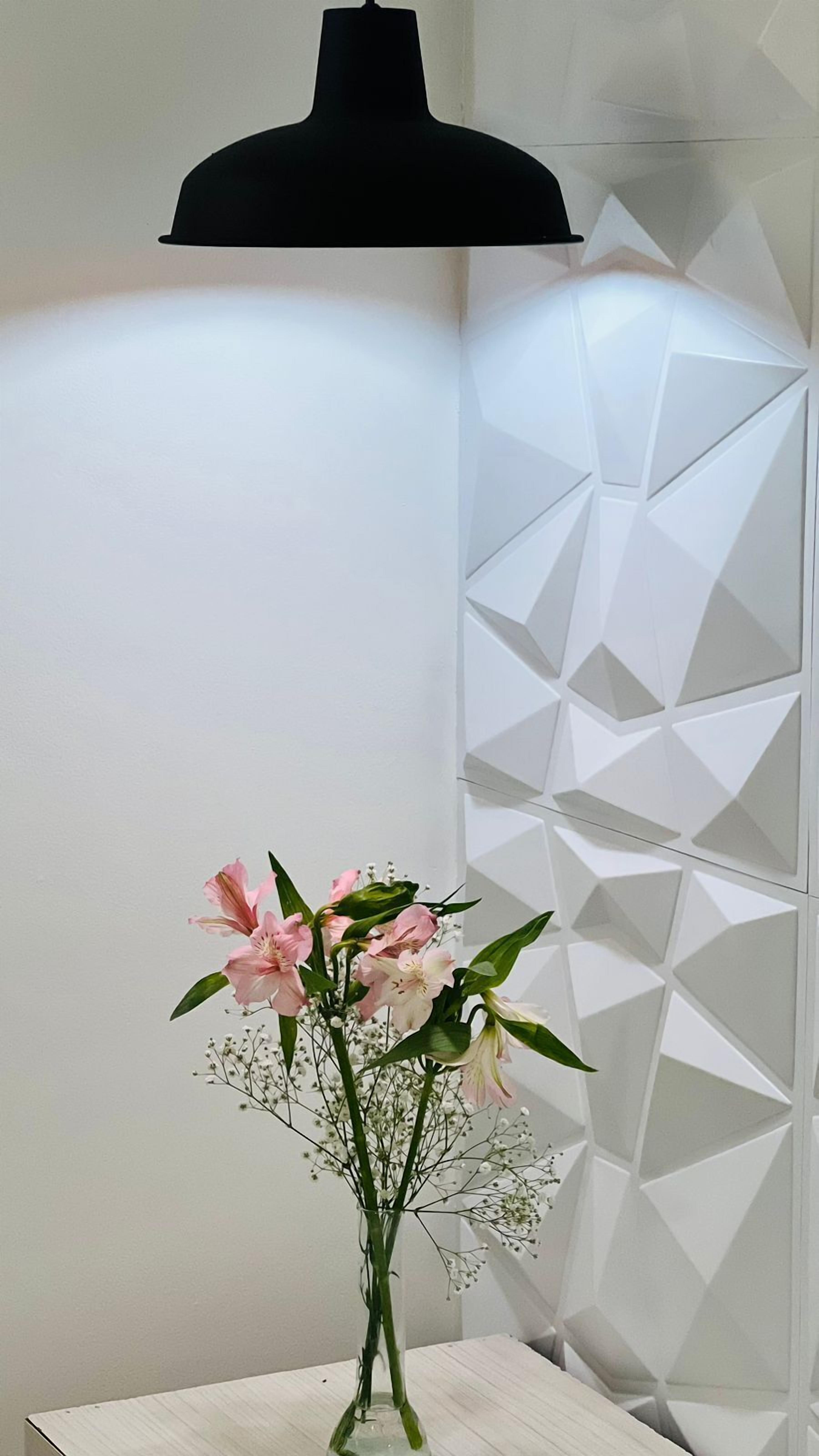 Une pièce avec un mur blanc et un séparateur à motifs géométriques. On peut voir un vase rempli de fleurs roses sur une table.