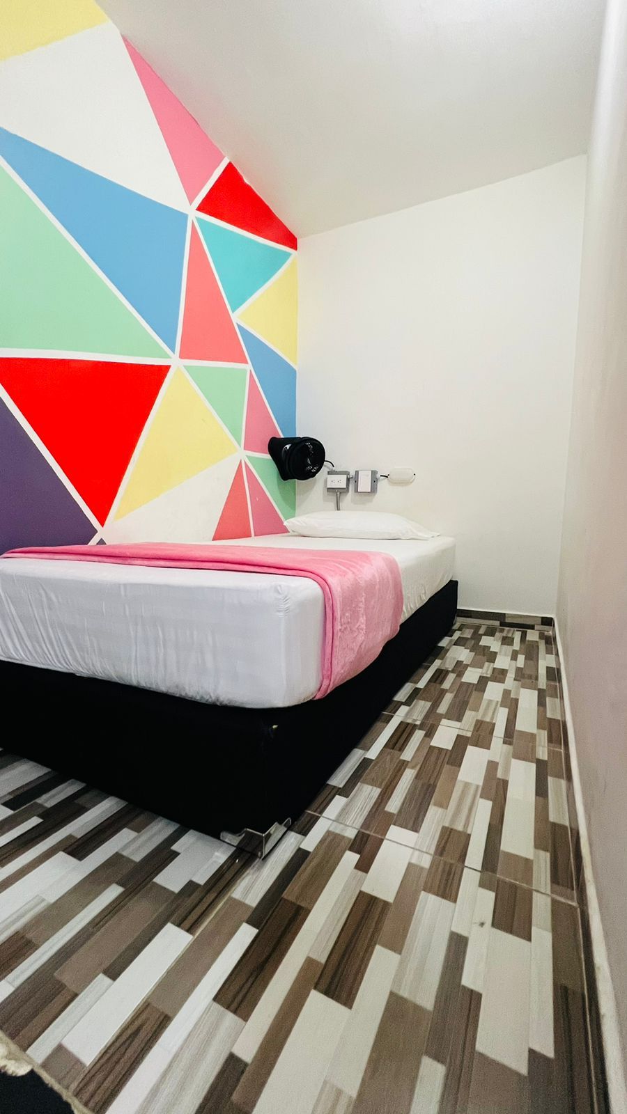 Un dormitorio con cama, mesita de noche, lámpara de pared y suelo estampado.