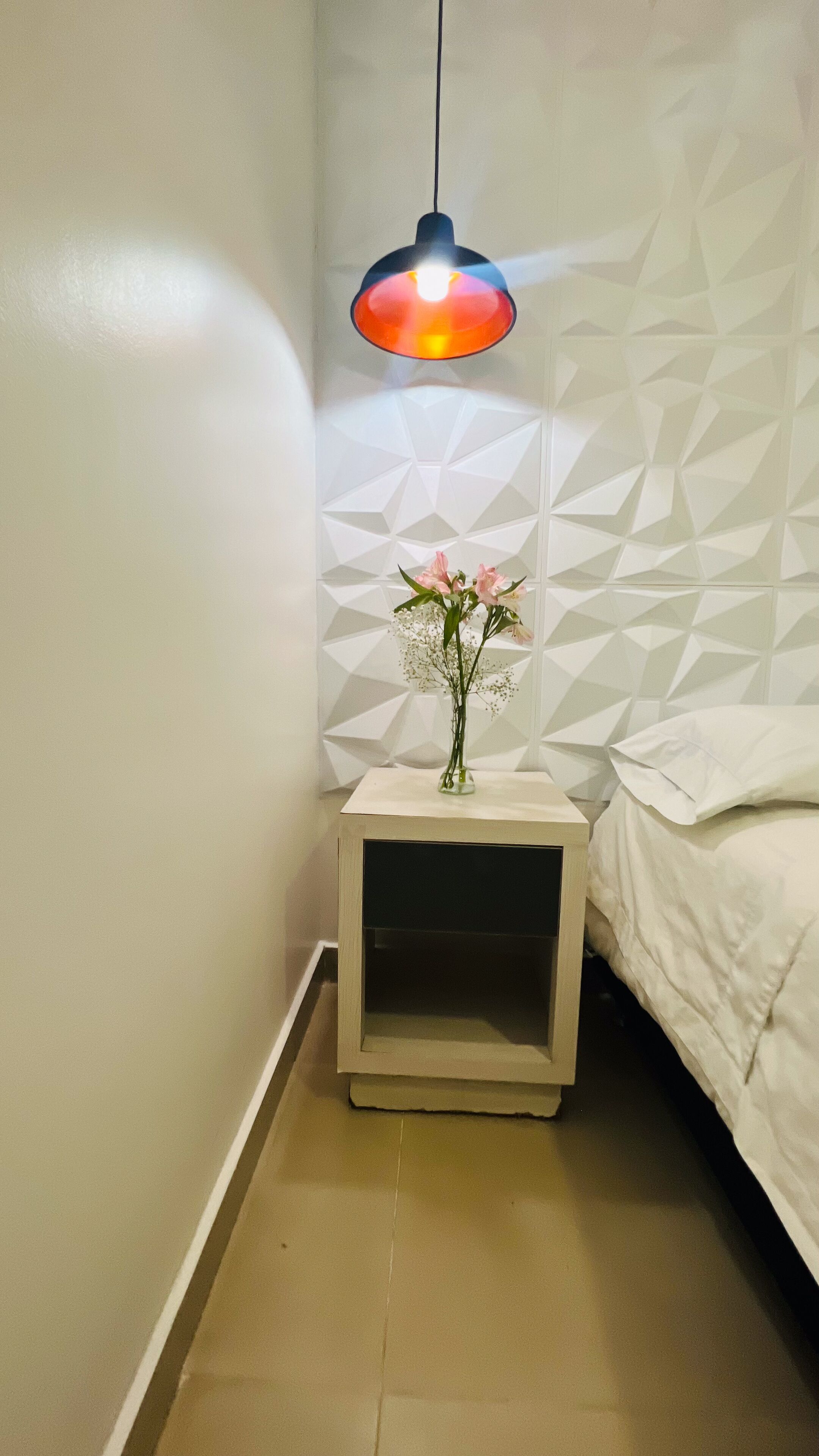 A small, neatly arranged bedroom with a bedside table, a lamp, and a bed.