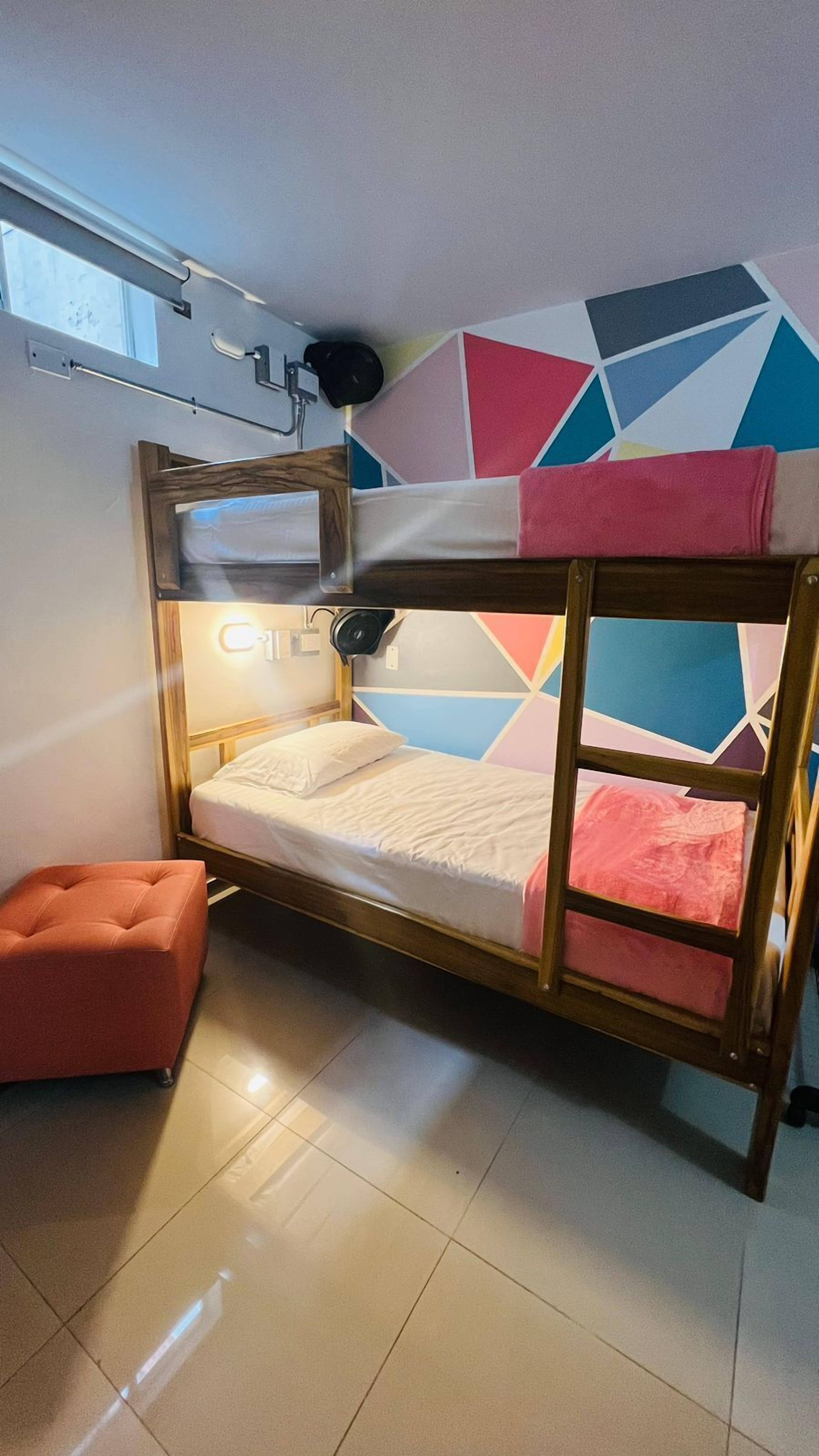 A bunk bed with a wooden frame, a pink cushion, and a colorful geometric-patterned wall.