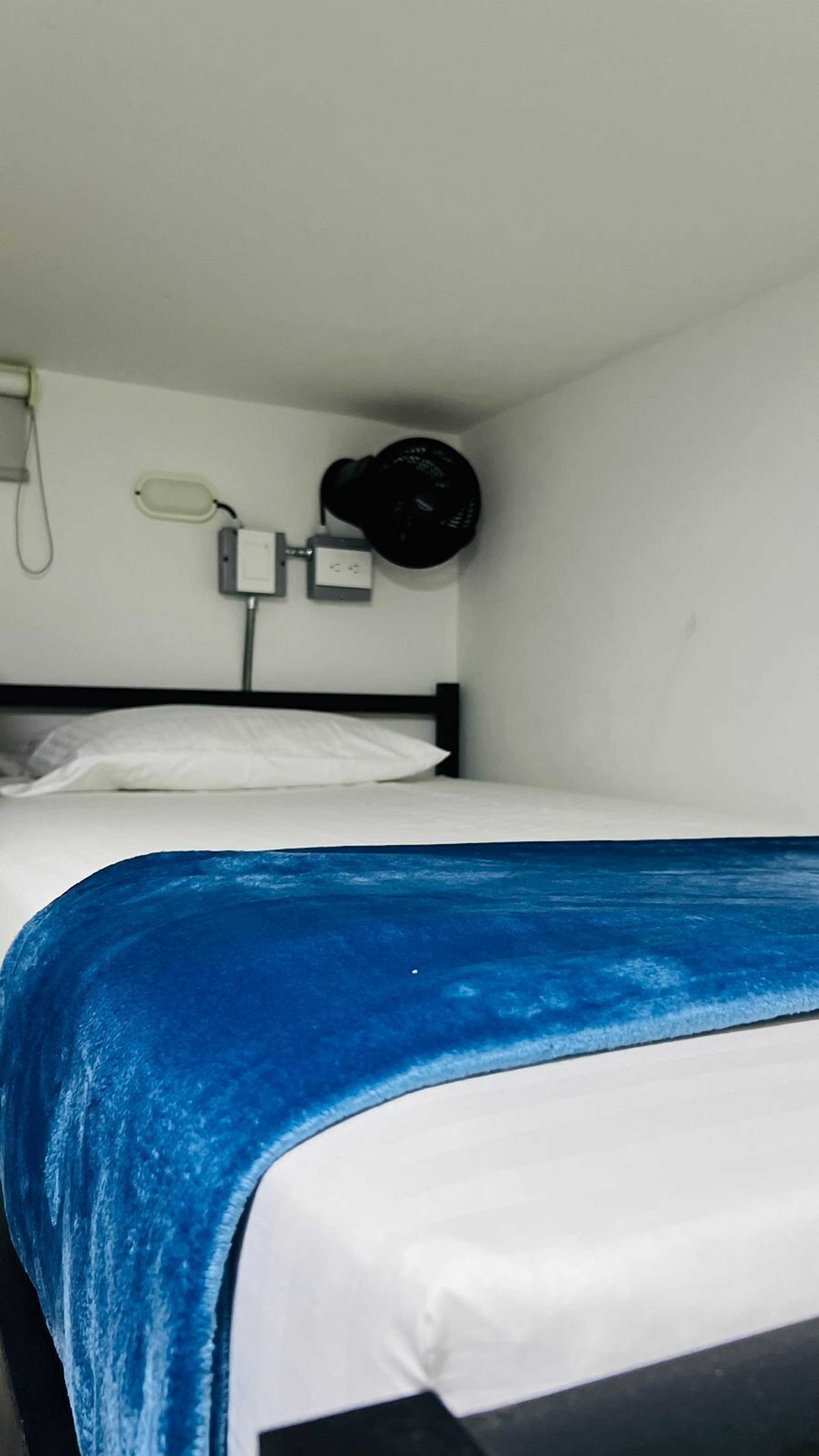 Una cama litera con colchón blanco y manta azul. Hay una lámpara de pared y un teléfono en la pared.