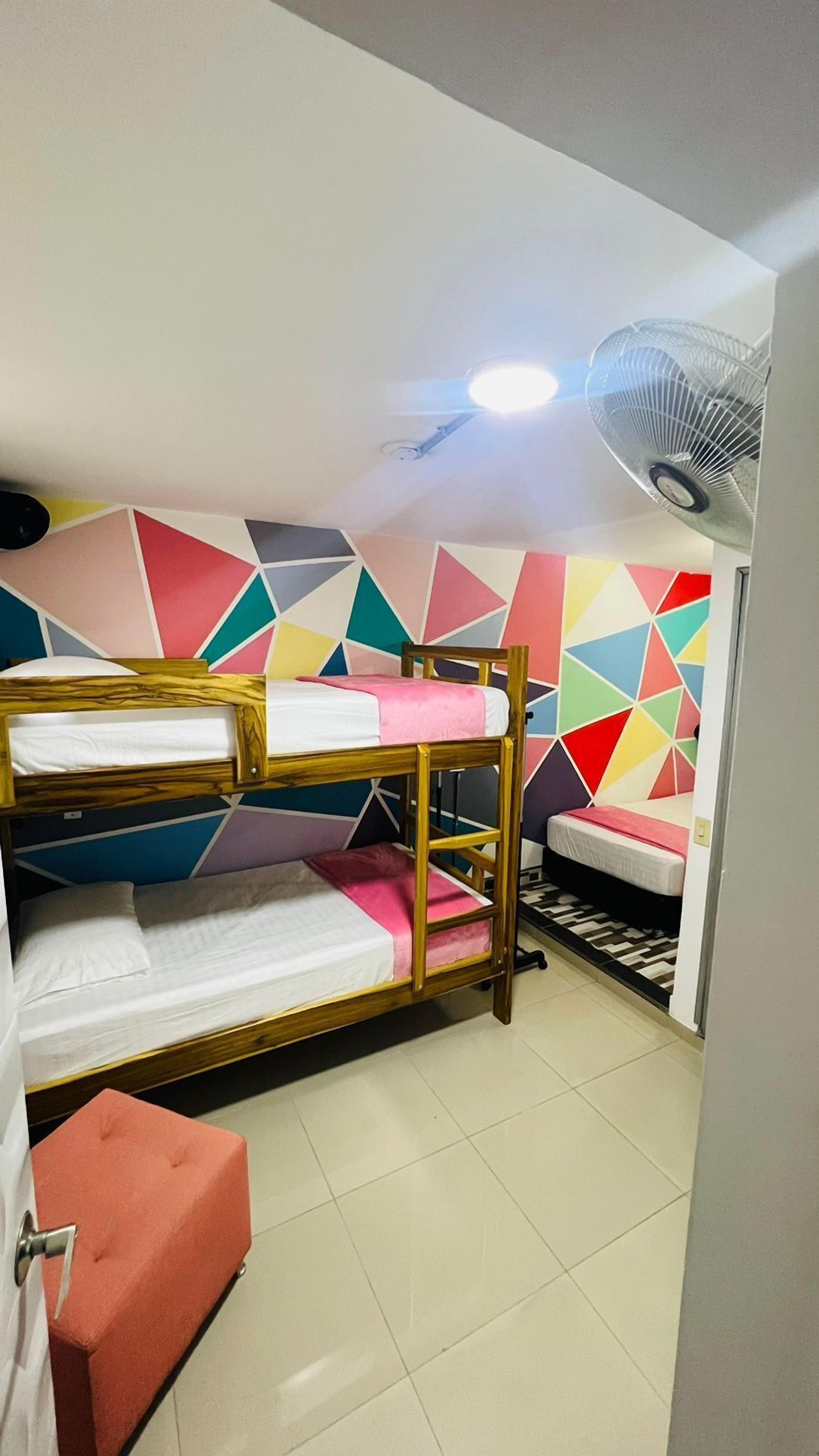 A dormitory room with bunk beds, a ceiling fan, and a colorful geometric wall design.
