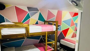 A dormitory room with bunk beds, a ceiling fan, and a colorful geometric wall design.