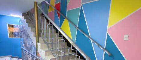A staircase with a metal railing, leading to a landing with a blue wall and geometric-patterned wall above.