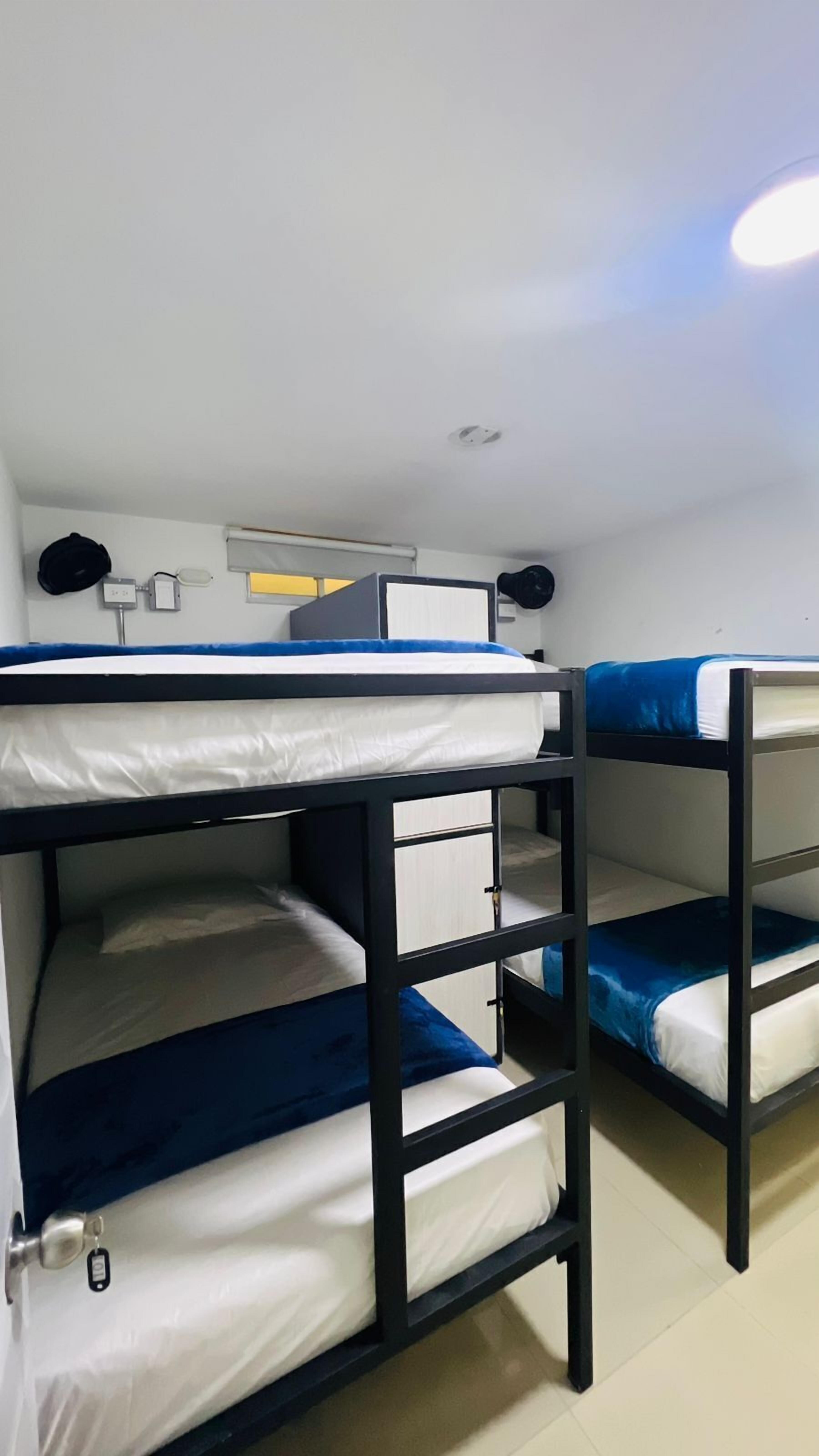 Une chambre avec un lit superposé, un plafond blanc, un luminaire apparent et une petite fenêtre avec un store.