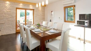 A dining area with a wooden table set for six, white chairs, and a view of the outdoors through a sliding door. - Villa Paradiso Zadarvillas (Policnik)