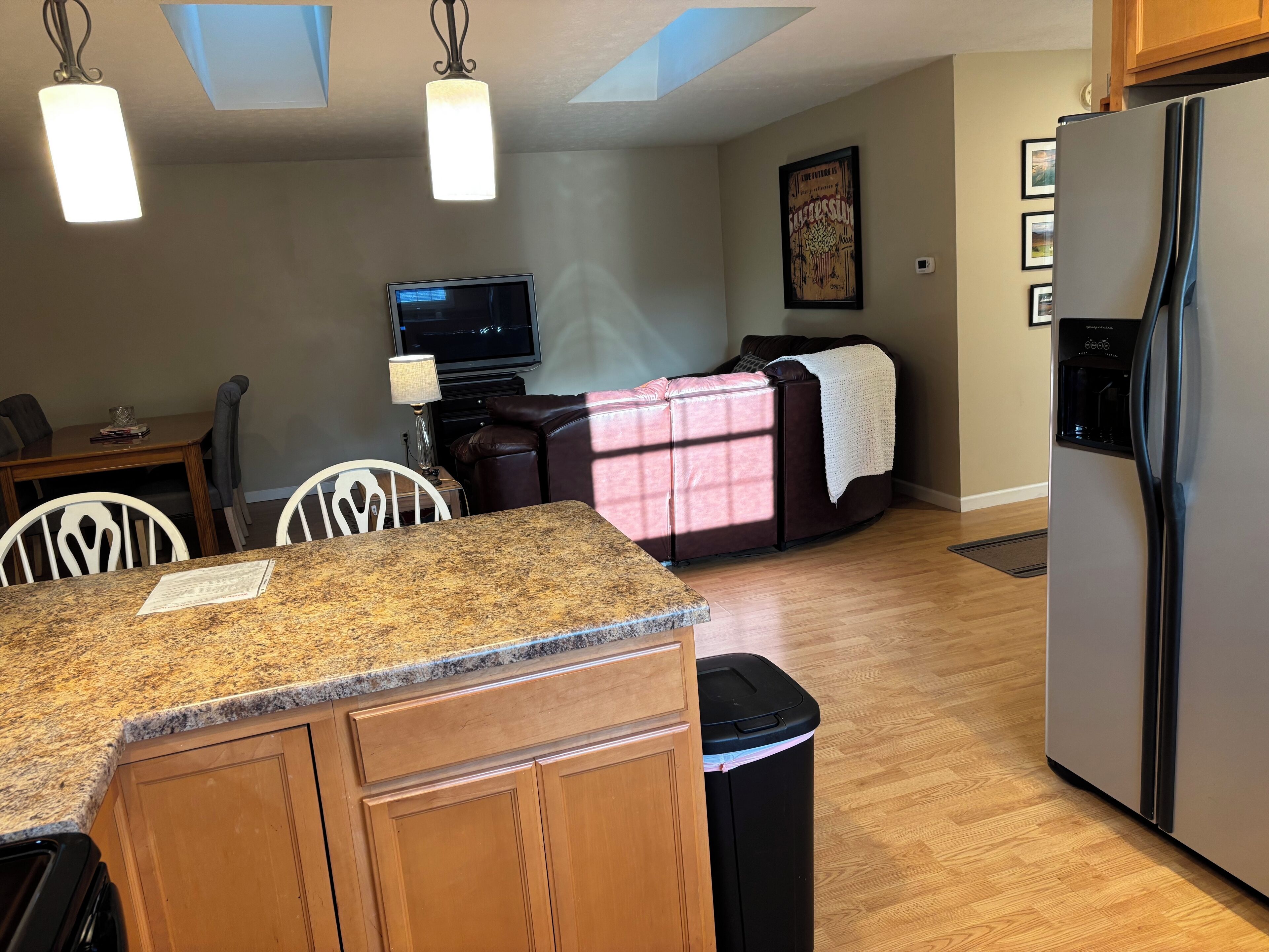 A modern kitchen with granite countertops, a stainless steel refrigerator, and a dining area with a table and chairs.