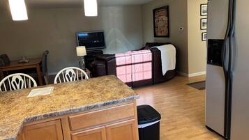 A modern kitchen with granite countertops, a stainless steel refrigerator, and a dining area with a table and chairs.
