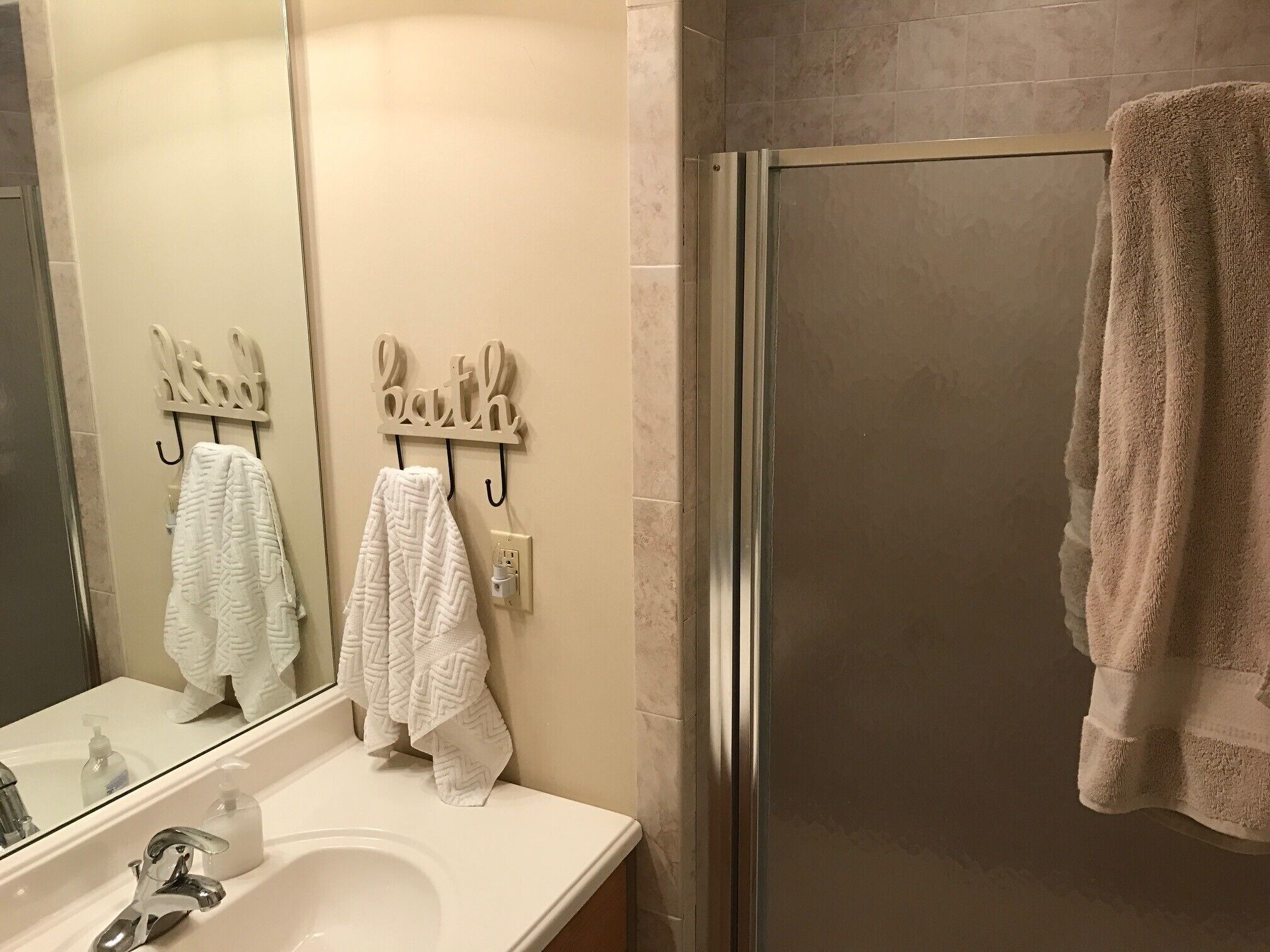 Une salle de bain avec un lavabo blanc, un miroir et deux serviettes suspendues à des crochets portant l’inscription « bain ».