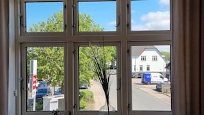 Una ventana con vista a una calle, un edificio blanco y una furgoneta estacionada.
