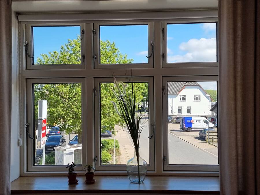 Une fenêtre donnant sur une rue, un immeuble blanc et un fourgon garé.