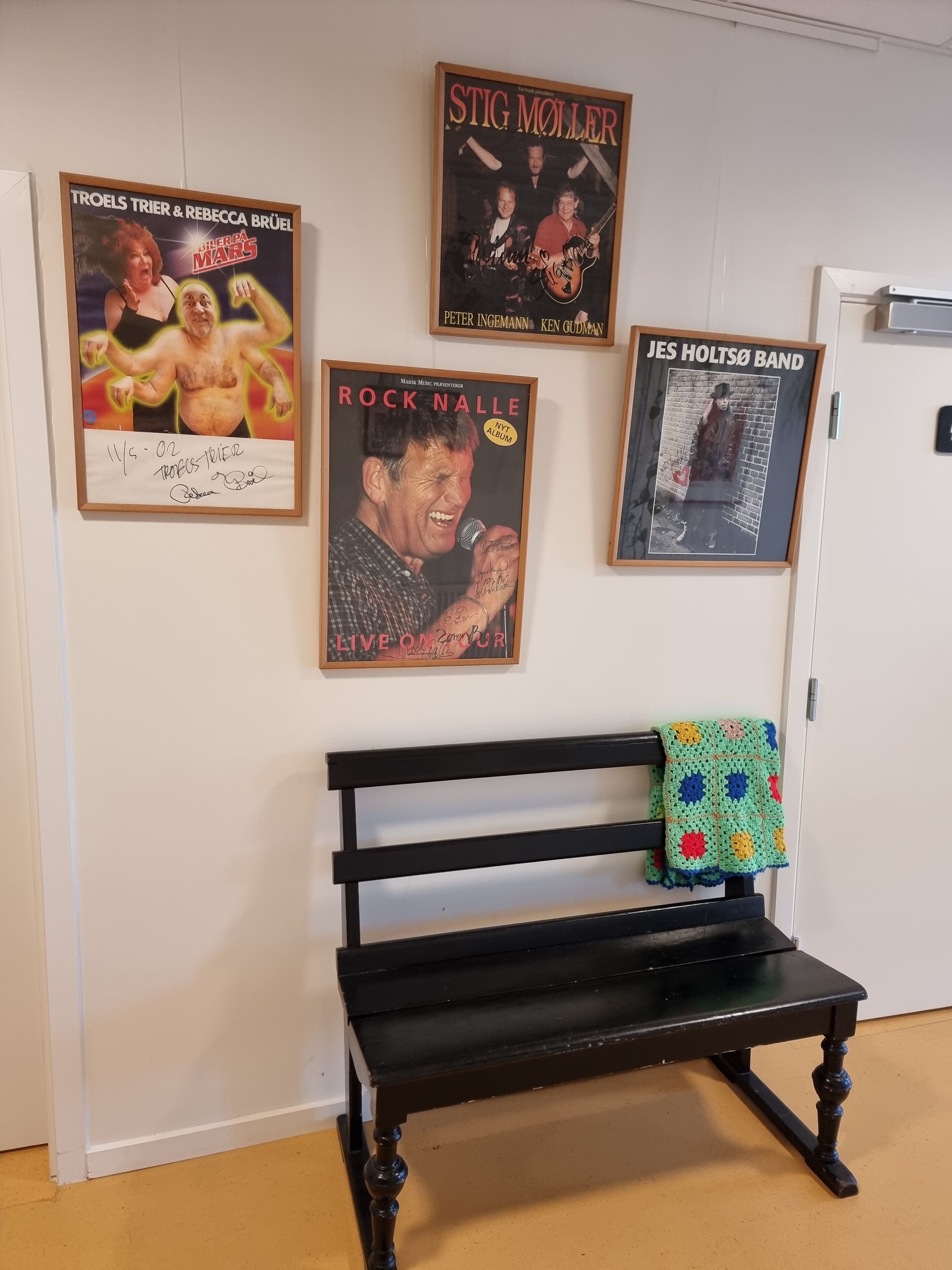 A room with a black bench, a white door, and four framed posters on the wall.