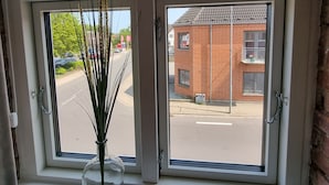 Una ventana de cuatro partes, un florero con cañas y una vista de un edificio de ladrillo y calle.