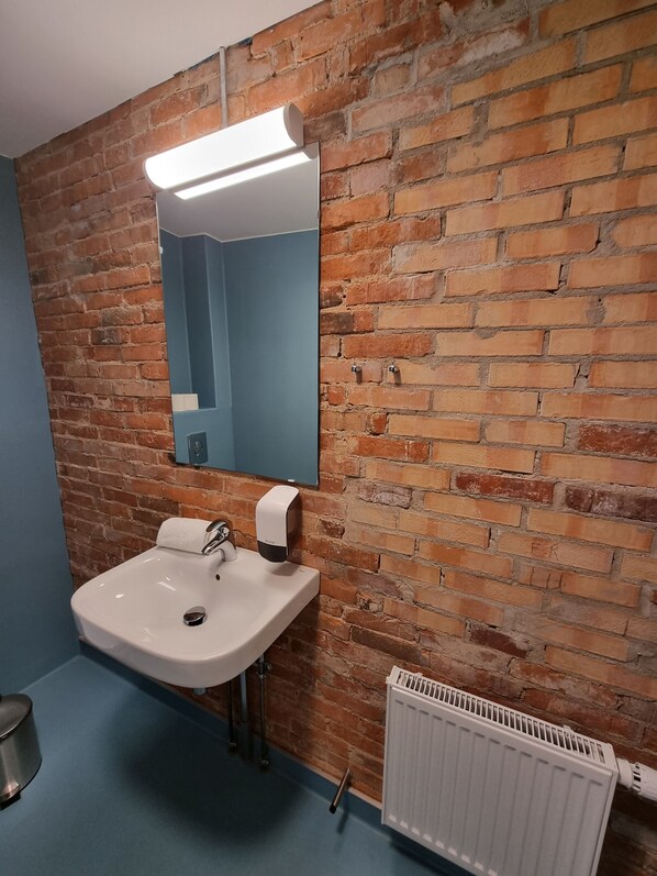 A bathroom with a white sink, a mirror, a soap dispenser, and a radiator. - Skovsgård Hotel (Brovst)