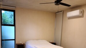 A bedroom with two beds, a ceiling fan, an air conditioning unit, and a window with a view of greenery. - Apartment Palma Comfort in Downtow, Pool (Mérida)