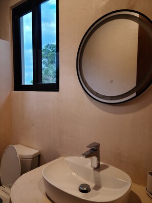 Een badkamer met een ronde spiegel, een wastafel en een toilet.