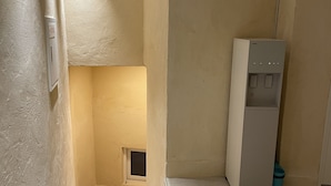 A small, narrow room with a white refrigerator, a blue trash bin, and a small window. - Hoho House (Busan)