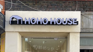 A hotel entrance with a glass door, a sign above reading "HOHO HOUSE", and a person standing inside. - Hoho House (Busan)