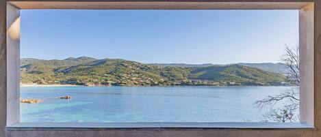 A room with a large window overlooking a coastal landscape with hills and a clear blue sea.