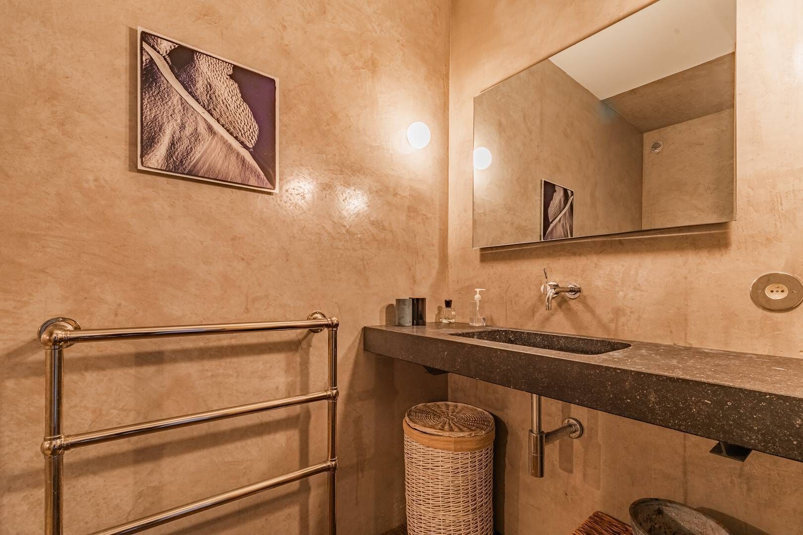 A bathroom with a towel rack, a sink, a mirror, a picture on the wall, and a wicker basket.