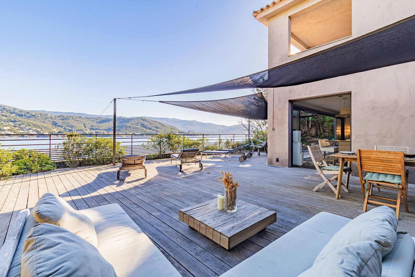 A wooden deck with outdoor seating, a table, and a view of a lake and mountains.