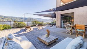 A wooden deck with outdoor seating, a table, and a view of a lake and mountains.