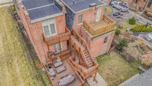 A two-story brick house with a wooden deck, outdoor seating, and a staircase leading to the upper level. - NEW! Brush Park Brilliance! Walk->Stadiums DT Luxe 3BR (Detroit)